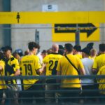 A vibrant crowd of football fans in yellow jerseys gathered at a stadium entrance during the day.