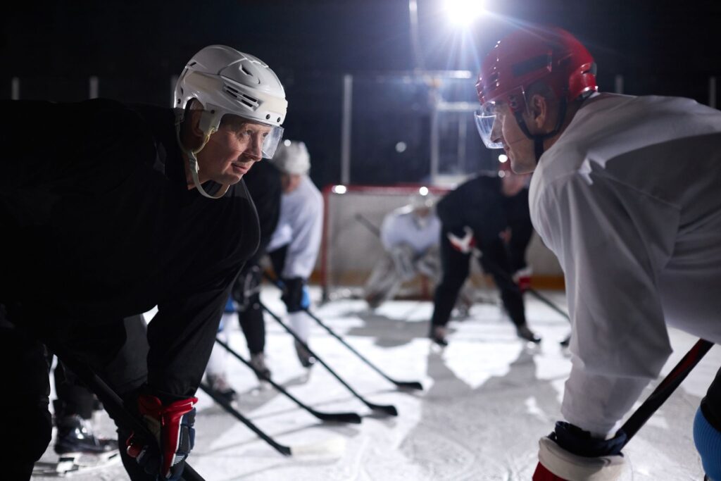 Two ice hockey players faceoff on a rink during a night game, surrounded by teammates in action.