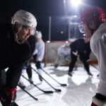 Two ice hockey players faceoff on a rink during a night game, surrounded by teammates in action.