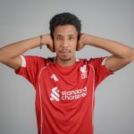 Portrait of a man wearing a red soccer jersey with a confident expression indoors.