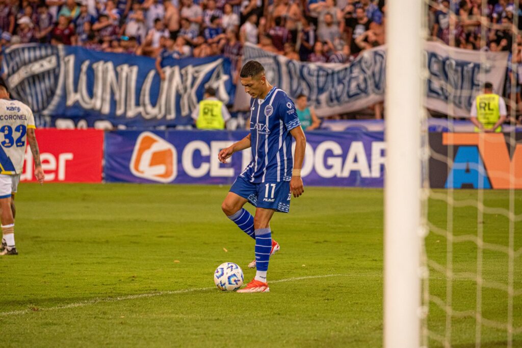 A soccer player in blue dribbles the ball during an outdoor football match.