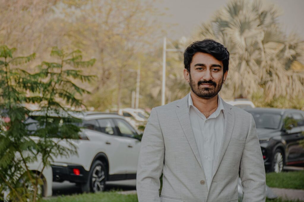 A man in a light suit standing outdoors in Islamabad, Pakistan, exuding confidence.