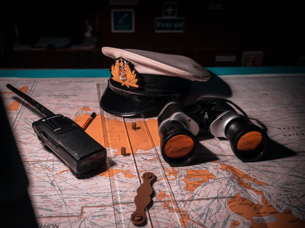 Close-up of ship captain's tools on a map, including hat, binoculars, and radio.