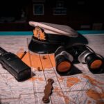Close-up of ship captain's tools on a map, including hat, binoculars, and radio.