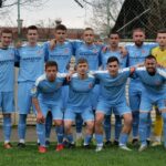 Group portrait of an amateur football team posing outdoors in blue jerseys.