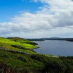 Beautiful coastal landscape in Ireland with rolling green hills and a calm blue sea under a cloudy sky.