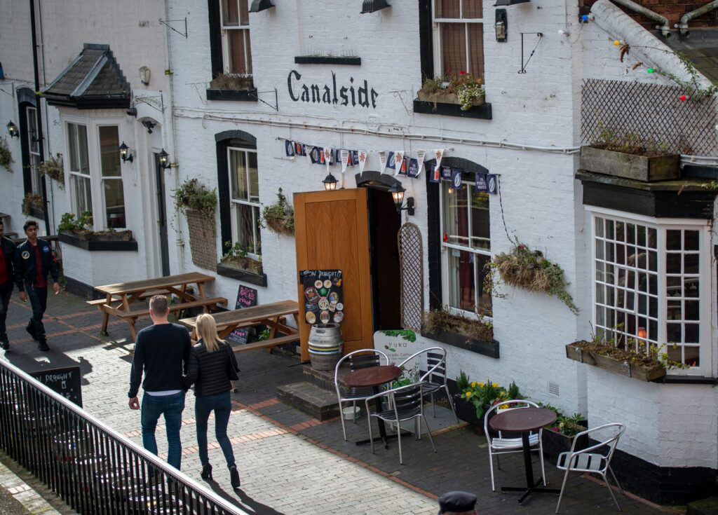 A quaint canal-side pub in Birmingham, England, with people enjoying a sunny day outdoors.