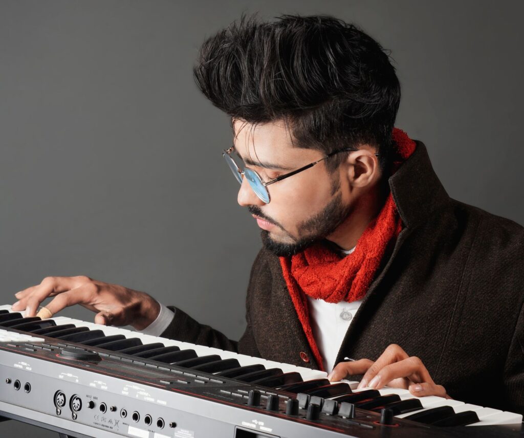 Man with glasses and red scarf playing an electronic piano intently.