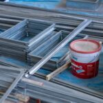 Stacks of metal frames and a paint bucket inside a construction site emphasizing building materials.