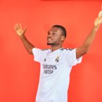 An enthusiastic football fan celebrating with arms raised in a jersey against a red background.