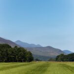 A serene view of the lush green fields and mountains of Killarney, Ireland under a clear blue sky.