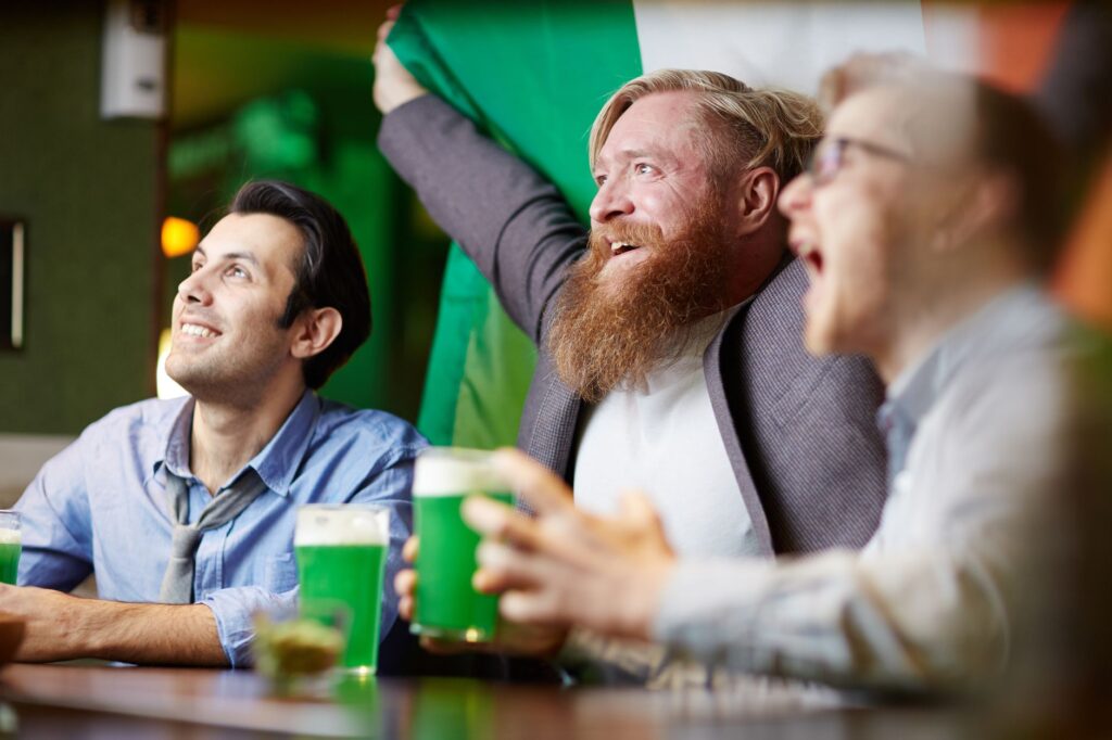 Enthusiastic friends celebrating St. Patrick's Day with green beer at a lively Irish pub.