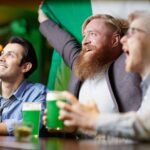 Enthusiastic friends celebrating St. Patrick's Day with green beer at a lively Irish pub.