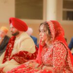 A bride and groom in traditional attire during an Indian wedding ceremony inside a venue.