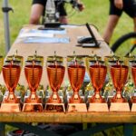 Bronze and gold trophies displayed on a wooden table at an outdoor cycling event in Estonia.