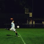 Dynamic action shot of a soccer player kicking the ball during a night game in Somerset, England.