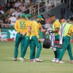 Cricket players gather on the field during a match, discussing strategy.