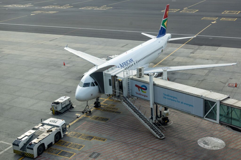 South African Airways aircraft docked at airport gate with passenger bridge connected.