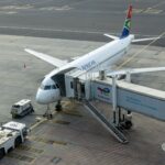South African Airways aircraft docked at airport gate with passenger bridge connected.