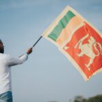 A man proudly waving the Sri Lankan flag outdoors under a clear sky.