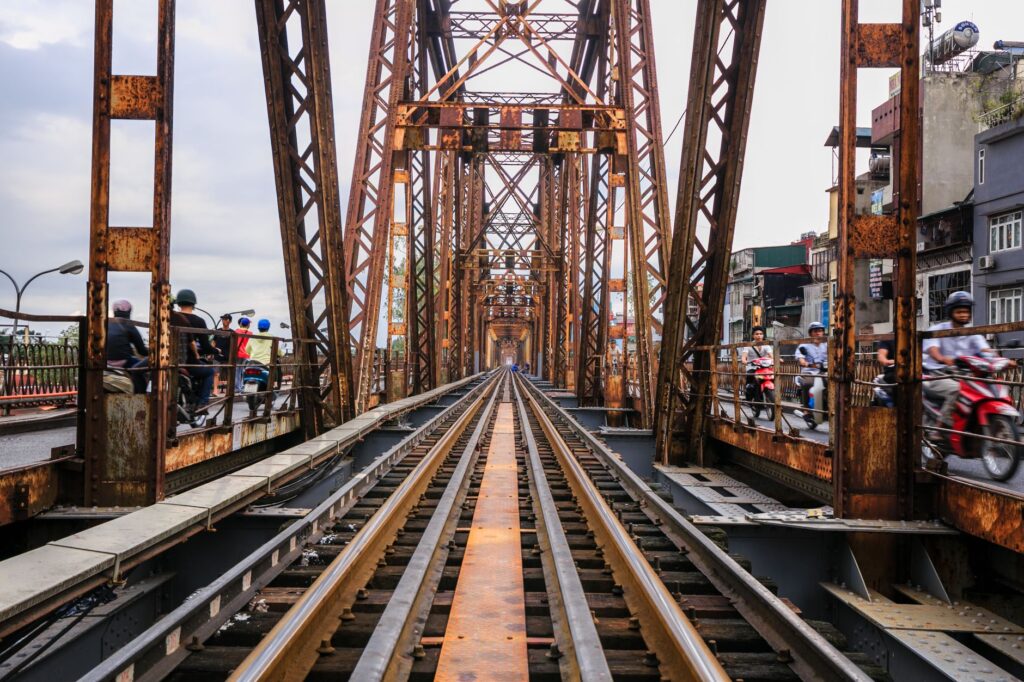 View down a rusty Iron bridge integrated with urban traffic and railways.