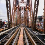 View down a rusty Iron bridge integrated with urban traffic and railways.