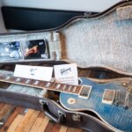 A Gibson electric guitar displayed in an open vintage case with documents.