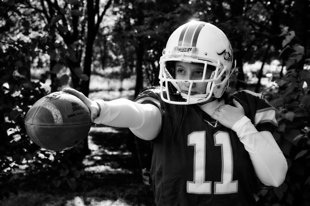 Black and white portrait of a female American football player outdoors holding a football.