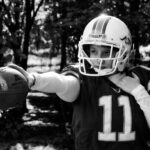 Black and white portrait of a female American football player outdoors holding a football.