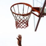 An upward view of a hand reaching for a basketball hoop on an outdoor court.