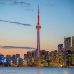 Beautiful sunset view of Toronto skyline with CN Tower and city lights reflecting on the lake.