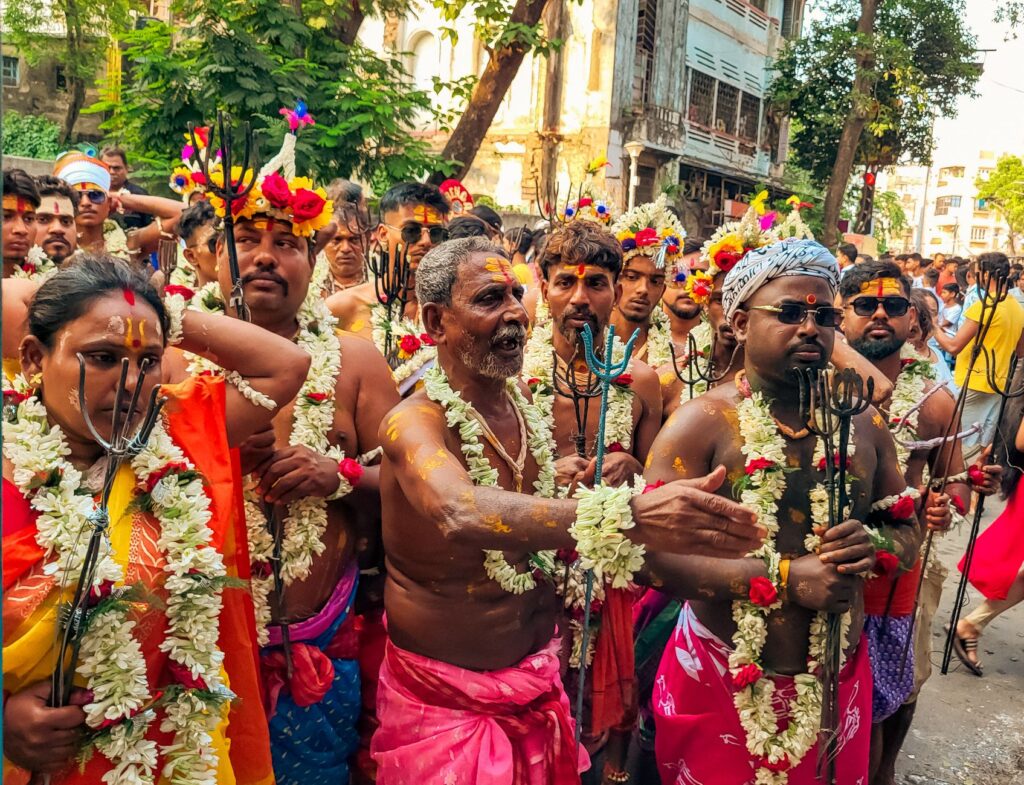 Colorful Hindu festival parade with traditionally dressed adults, floral garlands, and tridents in India.