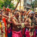 Colorful Hindu festival parade with traditionally dressed adults, floral garlands, and tridents in India.