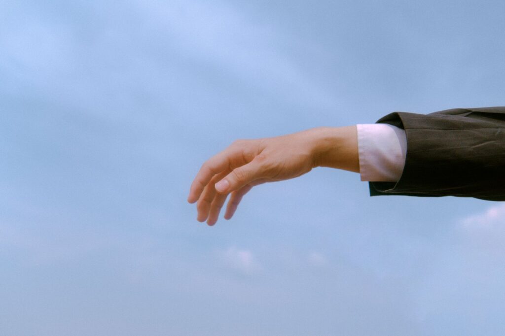 A businessman's hand reaching out against a blue sky, symbolizing opportunity and ambition.