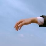 A businessman's hand reaching out against a blue sky, symbolizing opportunity and ambition.