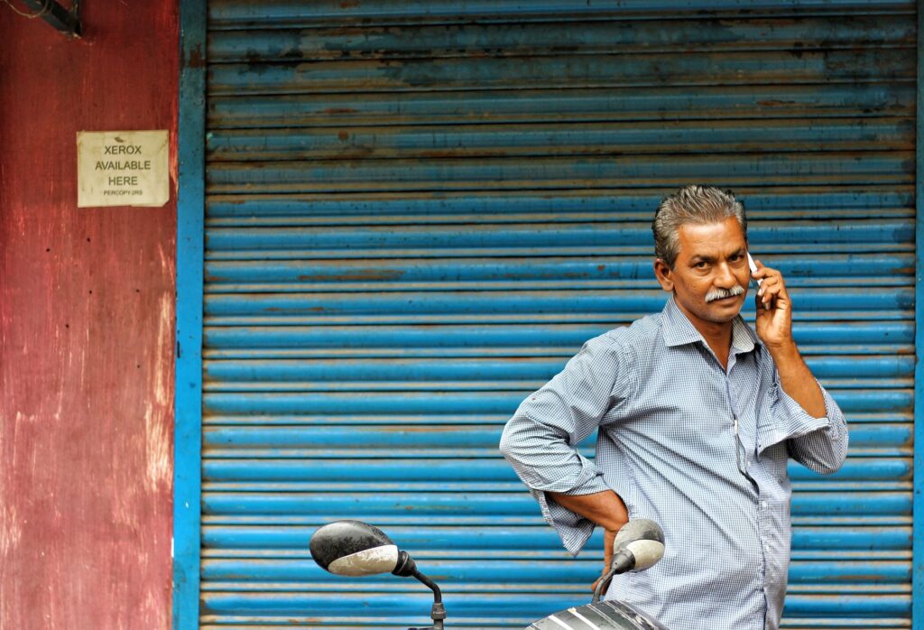 Middle-aged man on phone stands by closed shop shutter, mirror visible.