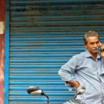 Middle-aged man on phone stands by closed shop shutter, mirror visible.
