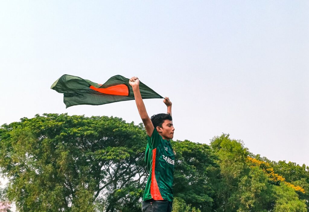A cricket fan passionately waving the Bangladesh flag outdoors under a clear sky, symbolizing national pride.