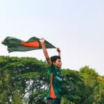A cricket fan passionately waving the Bangladesh flag outdoors under a clear sky, symbolizing national pride.