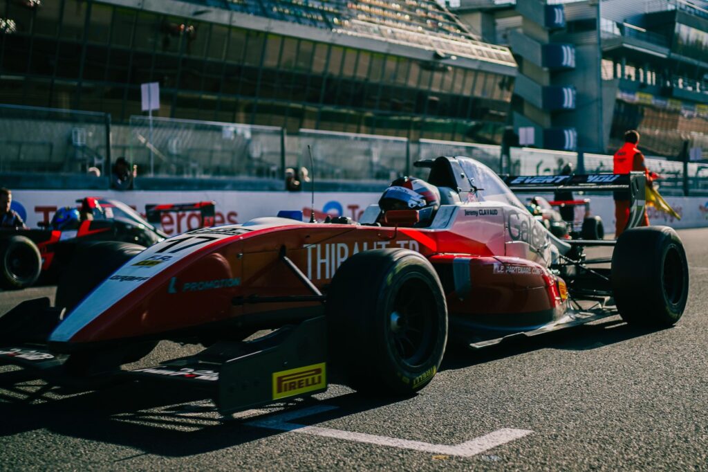 Close-up of a red Formula racing car on a track during a daytime event with spectators in the background.