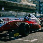 Close-up of a red Formula racing car on a track during a daytime event with spectators in the background.