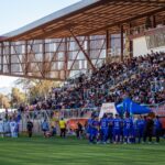 Packed stadium during a vibrant football game on a sunny day, showcasing team spirit and enthusiasm.