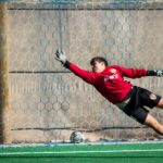 A dynamic shot of a soccer goalkeeper diving to save a ball at a local field in Chile.