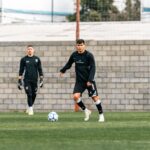 Two soccer players practicing on a field during daytime training session.