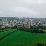 Aerial view capturing a vast green landscape with a charming town and historic architecture under a cloudy sky.