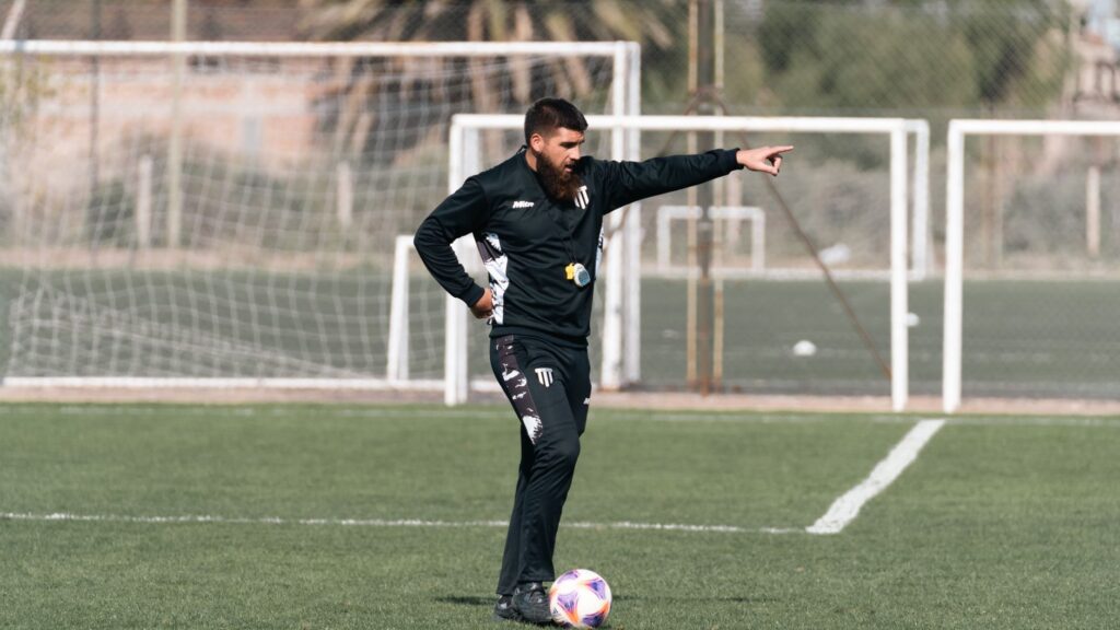 A soccer coach giving instructions during a practice session on an outdoor field.