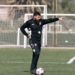 A soccer coach giving instructions during a practice session on an outdoor field.