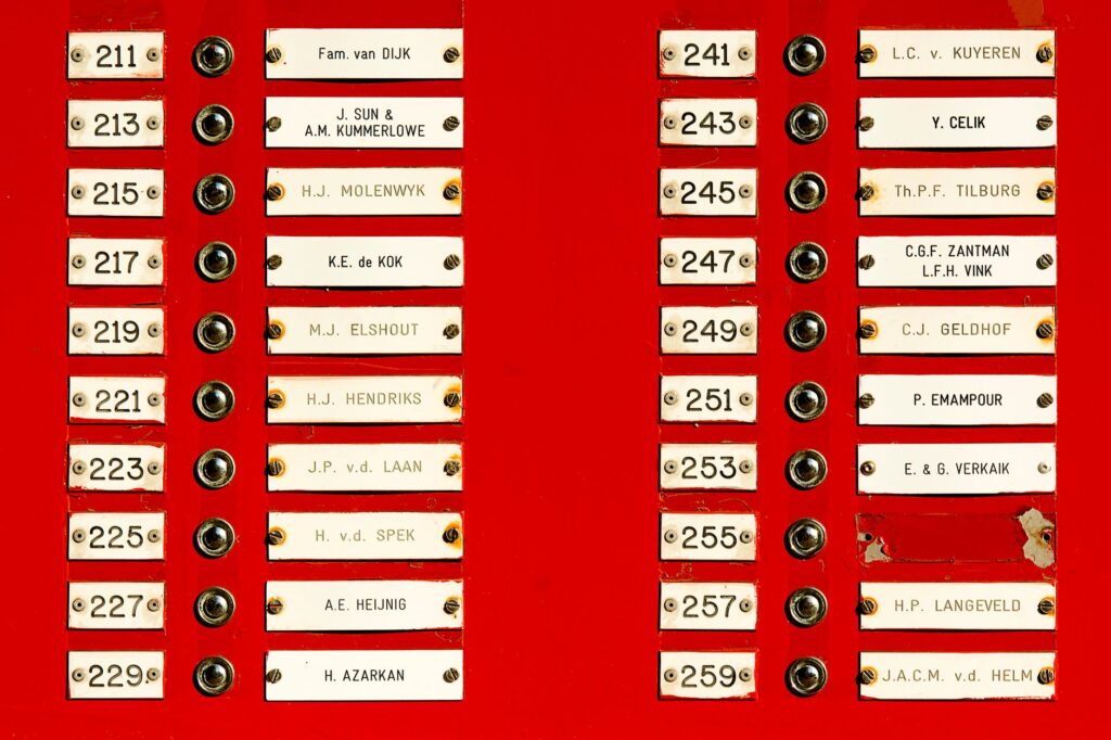 Close-up of a red doorbell panel with multiple nameplates and buttons in a building.