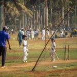 Young boys practicing cricket with coach in a Mumbai park. Sunny day, outdoor sports scene.