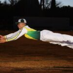 Cricketer in full sports gear leaps through the air to catch the ball, showing athleticism and focus.